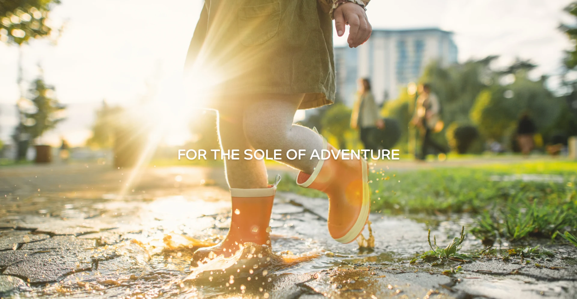 Child splashing through a puddle in orange WelliePaws boots