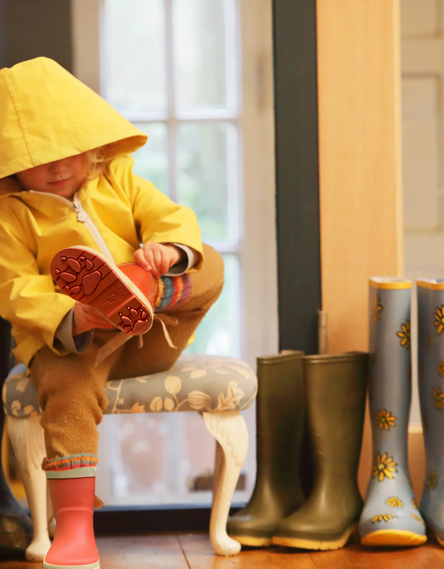 Child in a yellow raincoat sitting beside colourful WelliePaws boots