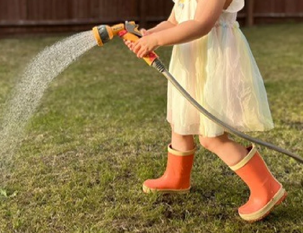 Child playing outdoors in orange wellington boots with a hose